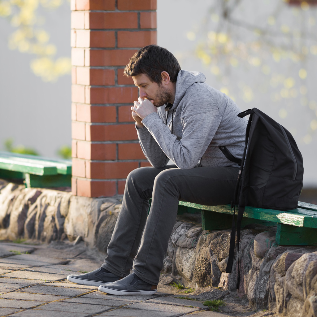 sad man sitting on a wooden bench outside thinking