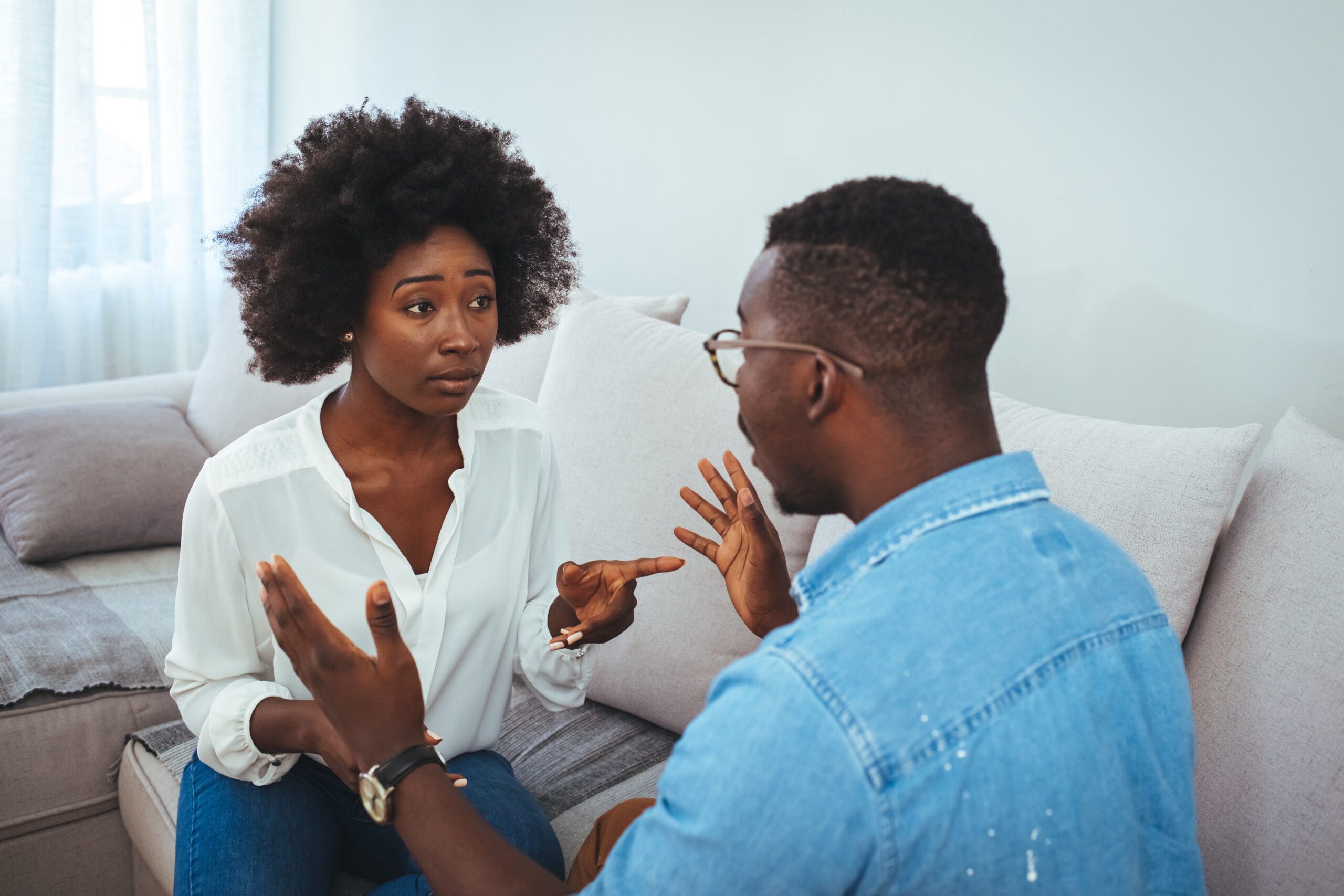 Angry young couple sit on couch in living room having family fight